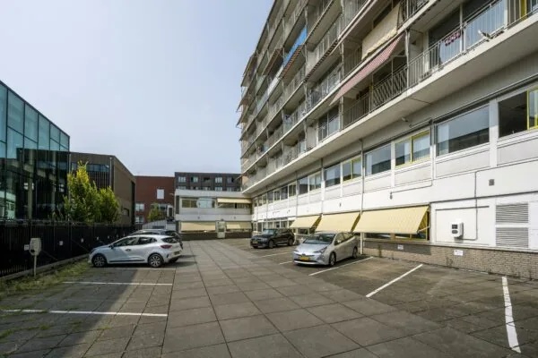 Parkeerplaats aan de Jan Tooropstraat met geparkeerde auto's naast een galerijflat en moderne kantoorgebouwen.